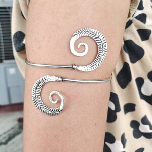 May include: Silver arm cuff with a spiral design. The cuff is made of two pieces of metal that are connected by a small hinge.