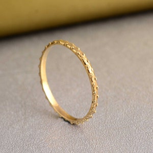 May include: A thin gold band ring with a textured surface of small dots.