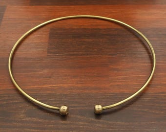 May include: A gold-toned metal choker necklace featuring a thin, circular wire band that remains open at the front. The two ends of the necklace are finished with small, smooth, spherical ball beads, creating a simple and clean design.