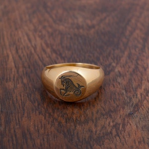 May include: A gold signet ring with a Capricorn zodiac symbol engraved on the top.