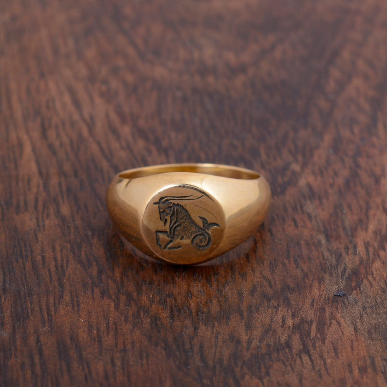 May include: A gold signet ring with a Capricorn zodiac symbol engraved on the top.