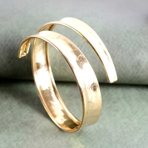 May include: A gold-toned metal bangle bracelet with a twisted design. The bracelet is made of two bands of metal that are intertwined.