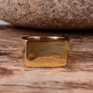 Op de afbeelding: Een vierkante signet ring van goudkleur met een glad, gepolijst oppervlak.