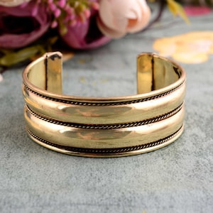 May include: A gold-toned metal bangle bracelet with a double-row design. The bracelet has a smooth, polished finish and a slightly rounded shape.