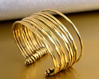 May include: A gold-toned bangle bracelet made of multiple thin, hammered metal bands. The bracelet is open and adjustable.