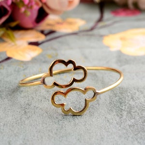 May include: A gold-toned metal bracelet featuring a cloud design. The bracelet is open and has a simple, minimalist style.