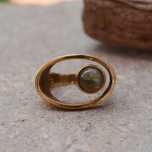 Può includere: Un anello d'oro con una pietra preziosa rotonda e verde incastonata in una cornice ovale unica.