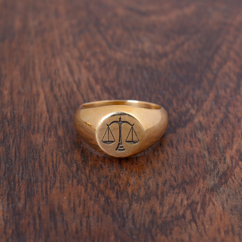 May include: A gold signet ring with a scale of justice design.