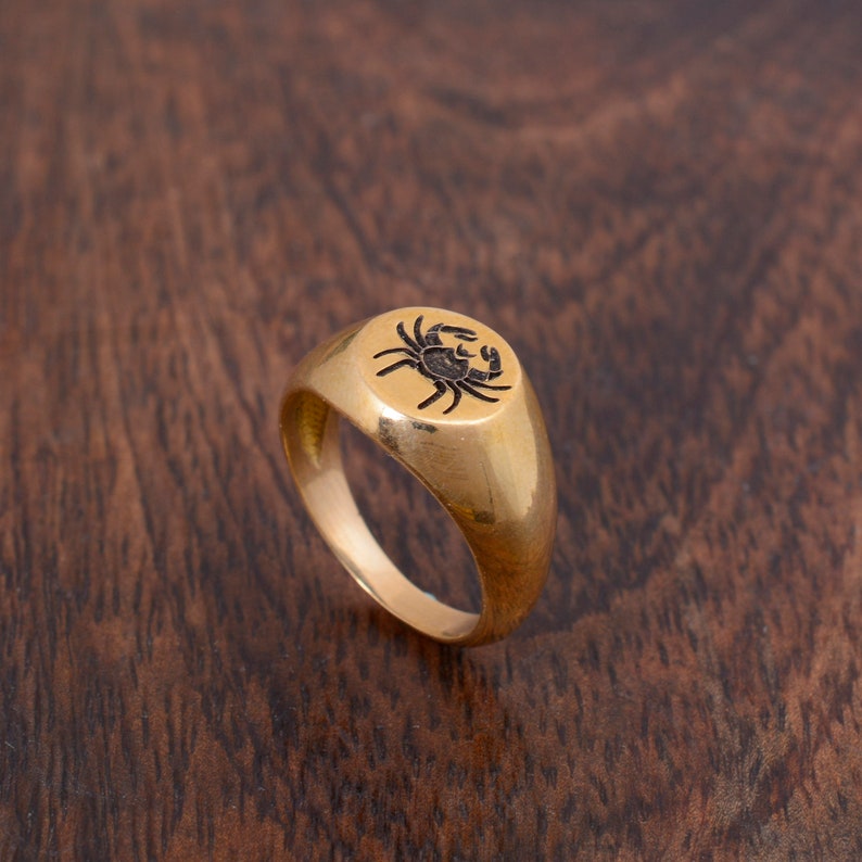May include: A gold signet ring with a black crab design on the top.