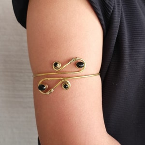 May include: Gold arm cuff with a delicate design and black beads. The cuff is open and adjustable.
