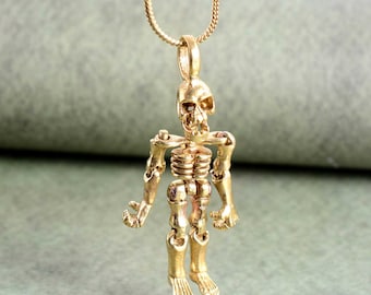May include: A gold skeleton pendant necklace. The skeleton is articulated and has a detailed skull. The necklace is on a gold chain.