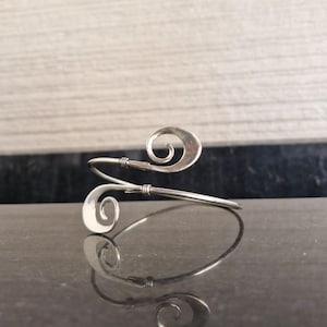 May include: A silver bracelet with a unique design featuring two spiral shapes. The bracelet is made of thin metal and has a delicate look.