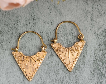 Peut inclure: Une paire de boucles d'oreilles créoles en forme de triangle dorées avec un motif géométrique. Les boucles d'oreilles sont en métal et ont une finition brillante.