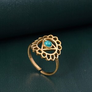May include: Gold ring with a turquoise stone set in a triangle design surrounded by a decorative mandala-like pattern.