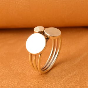 May include: A gold ring with three stacked circles. The largest circle is in the center and the two smaller circles are on either side of it.
