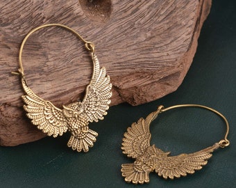 May include: A pair of gold-toned hoop earrings with an owl design. The owls have detailed wings and are facing forward.