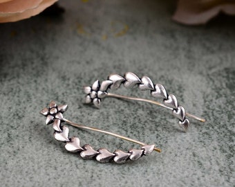 May include: A pair of silver ear cuffs with a flower design and a row of hearts. The cuffs are made of metal and have a delicate, feminine look.