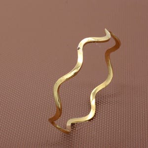 Op de afbeelding: Een golvende armband van goudkleurig metaal. De armband is gemaakt van dun metaal en heeft een eenvoudig, elegant ontwerp.