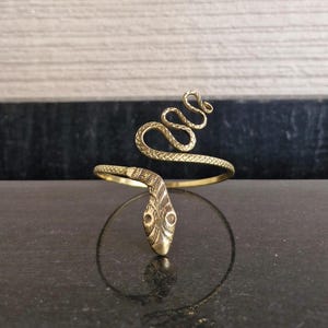 May include: A gold-toned snake bracelet with a coiled snake design. The snake's head is facing forward with detailed eyes and scales.
