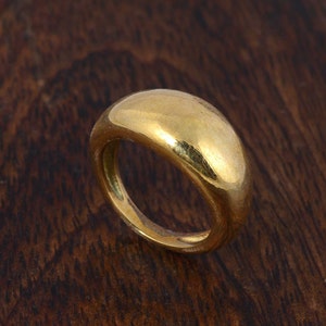 Op de afbeelding: Een eenvoudige gouden ring met een afgeronde, gladde bovenkant. De ring is gemaakt van gepolijst goud en heeft een klassiek ontwerp.