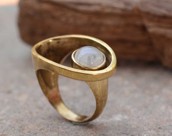 Könnte beinhalten: Ein goldener Ring mit einem großen, runden, weißen Edelstein, der in einem einzigartigen, offenen Design gefasst ist.
