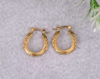 May include: A pair of gold hoop earrings featuring a textured, engraved pattern along the surface. The earrings have a hinged closure mechanism at the top, allowing them to open and close securely. The metal has a polished, reflective finish.