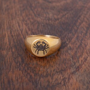 May include: A gold signet ring with a black crab design.
