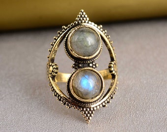 Può includere: Un anello d'oro con due pietre di luna rotonde iridescenti incastonate in un design decorativo e ornato.