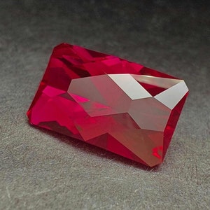 May include: A deep red gemstone with a rectangular cut and many facets.