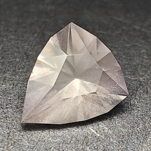 以下が含まれることがあります： 薄いピンク色の三角形のファセットカットの宝石。宝石はハート型にカットされており、滑らかで磨かれた仕上げになっています。