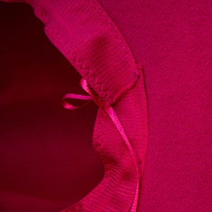 Puede incluir: Primer plano del interior de un sombrero rosa brillante. El sombrero tiene una cinta cosida en la costura interior, atada en un lazo.