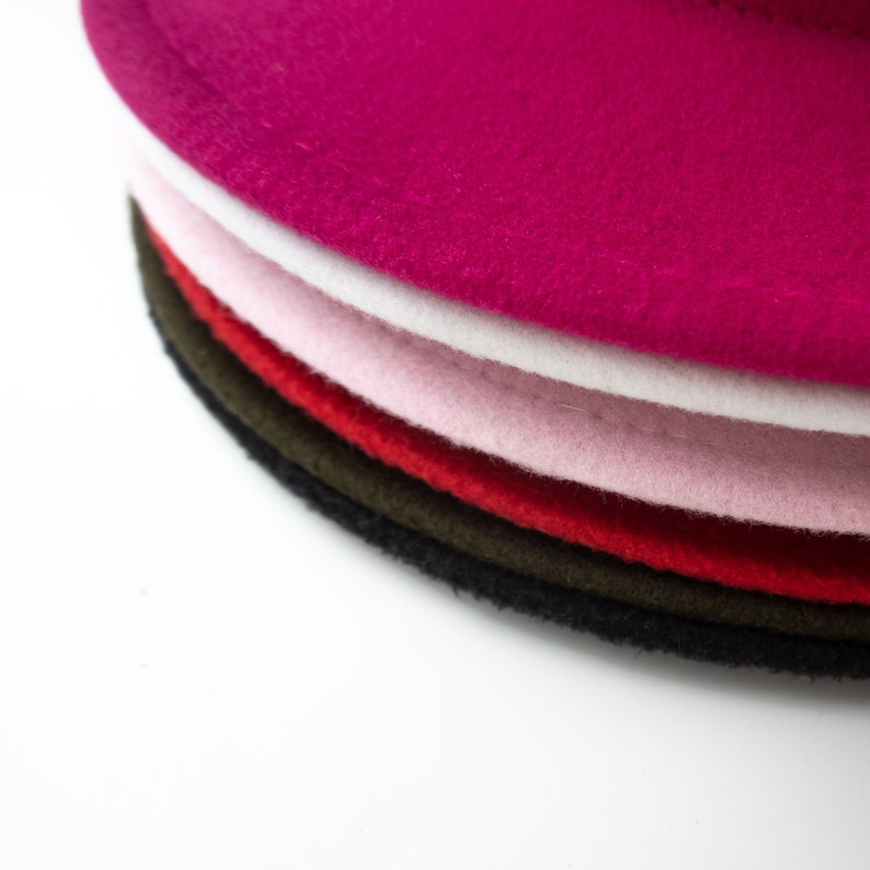 Puede incluir: Una pila de seis boinas de fieltro en varios colores, incluyendo rosa, blanco, rojo, verde y negro.