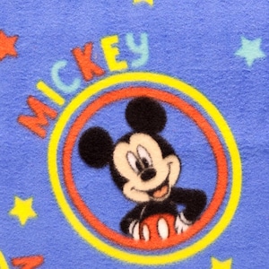 K&ouml;nnte beinhalten: Blauer Stoff mit einem sich wiederholenden Muster von Mickey Mouse in einem gelben und roten Kreis mit dem Wort "Mickey" in gelben Buchstaben. Der Hintergrund ist blau mit gelben Sternen.