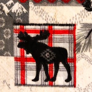 May include: A black moose silhouette on a white background with a red and gray plaid pattern. The moose is standing on a white background with a red and gray plaid pattern.