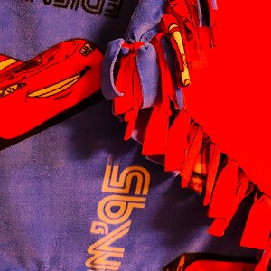 May include: A blue and red fleece blanket with the words "Friends" and "Lightning McQueen" printed on it. The blanket has fringe on all sides.
