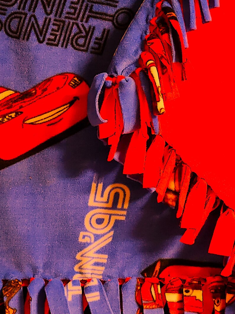 May include: A blue and red fleece blanket with the words "Friends" and "Lightning McQueen" printed on it. The blanket has fringe on all sides.