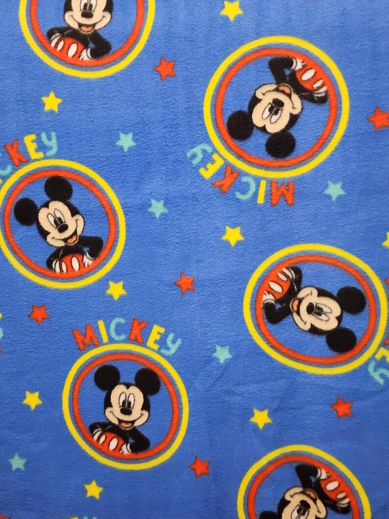 K&ouml;nnte beinhalten: Blauer Stoff mit einem sich wiederholenden Muster von Mickey Mouse in einem gelben, roten und orangen Kreis. Die Worte "Mickey" sind in einem gelben, roten und orangen Bogen um den Kreis geschrieben. &Uuml;ber den Stoff sind kleine gelbe und rote Sterne verteilt.