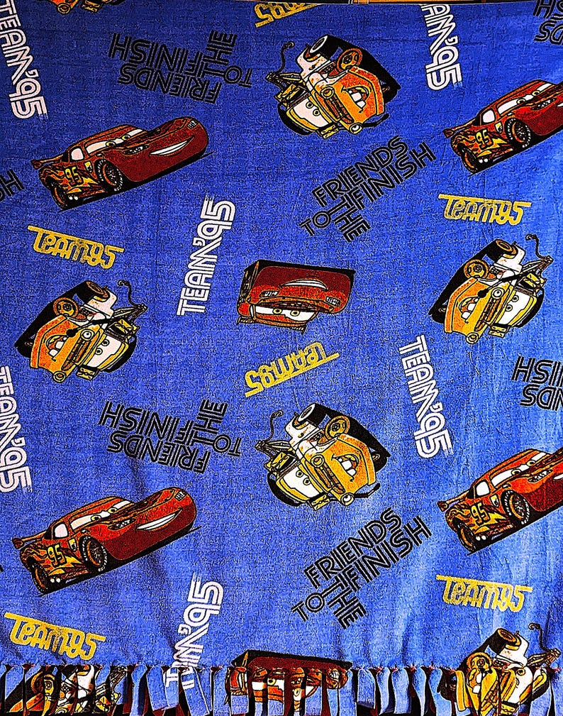 May include: Blue fleece blanket with a Cars theme. The blanket features images of Lightning McQueen and Mater, along with the text "Friends to the Finish" and "Team 95".