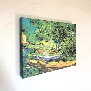 Pode incluir: Uma pintura que representa uma cena de rio com vários barcos atracados ao longo da margem. Os barcos são pintados em várias cores, incluindo azul, verde e amarelo. O rio é de um verde vibrante, e as árvores ao longo da margem são de um verde exuberante. Há duas figuras em pé na margem, uma com uma camisa azul e a outra com um vestido branco.