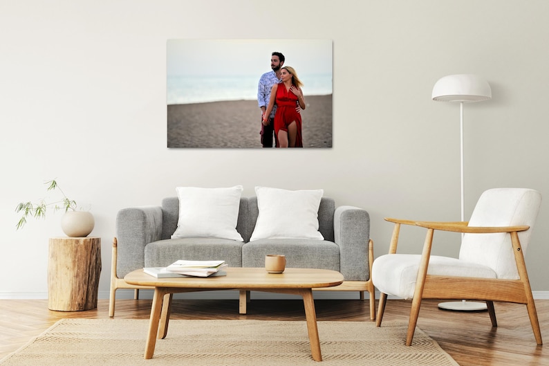 Puede incluir: Una pareja posa para una foto en una playa. El hombre lleva una camisa azul y la mujer lleva un vestido rojo. La playa es arenosa y el agua est&aacute; en el fondo.