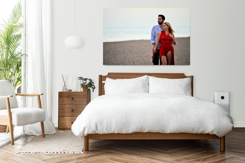 Puede incluir: Una pareja camina de la mano en una playa de arena. La mujer lleva un vestido rojo y el hombre lleva una camisa azul y blanca con estampado. La pareja est&aacute; enmarcada por una pared blanca y una cama blanca con ropa de cama blanca.