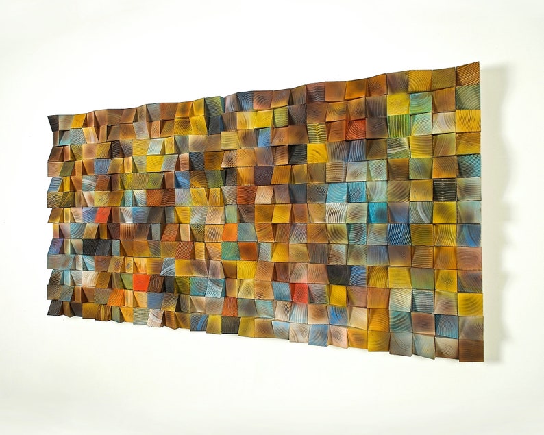 May include: A wall art piece made of wood with a mosaic of different colored wood squares. The squares are arranged in a wave pattern and are all different sizes. The colors are mostly shades of brown, yellow, and blue.