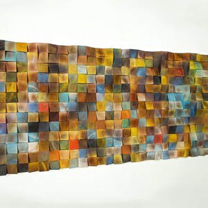 May include: A wall art piece made of wood blocks in various shades of brown, blue, yellow, and red. The blocks are arranged in a grid pattern and create a textured, abstract design.
