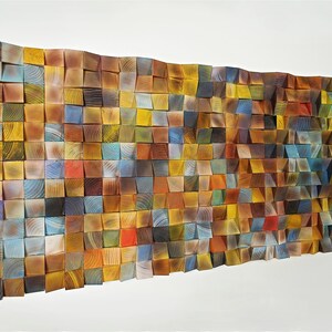 May include: A wall art piece made of wood blocks in various shades of brown, yellow, blue, and green. The blocks are arranged in a grid pattern and create a textured, abstract design.