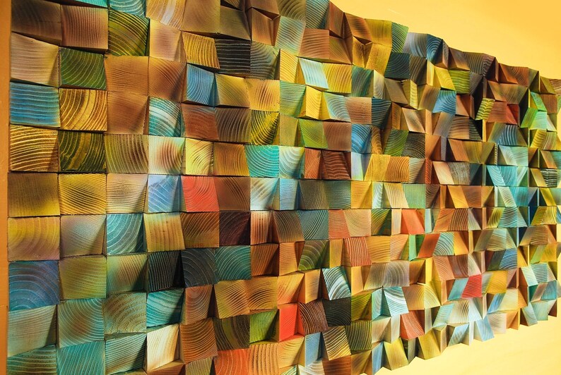 May include: A wall art piece made of wood blocks in various shades of brown, blue, green, and red. The blocks are arranged in a geometric pattern, creating a textured and visually interesting surface.
