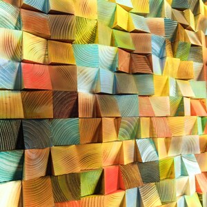 May include: A wall art piece made of colorful wooden blocks arranged in a geometric pattern. The blocks are stained in shades of blue, green, yellow, orange, and red.