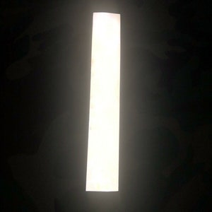 May include: A white reflective strip, commonly used for safety purposes, is illuminated by a light source.