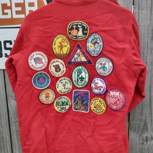 Peut inclure: Veste en laine rouge avec divers patchs brodés, dont "Keep America Beautiful", "Scout-O-Rama", "East Carolina Council" et "Catholic Retreat".