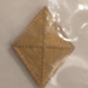 Puede incluir: Un parche de color dorado en forma de diamante con un diseño cosido.