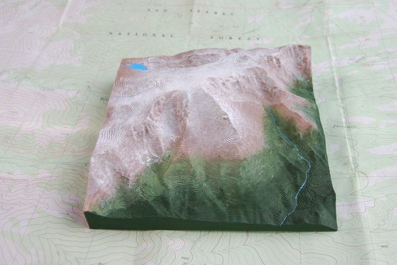 K&ouml;nnte beinhalten: Ein 3D-Modell einer Bergkette mit schneebedeckten Gipfeln und gr&uuml;nen T&auml;lern. Das Modell besteht aus einem strukturierten Material und ist in Braun-, Gr&uuml;n- und Wei&szlig;t&ouml;nen bemalt.